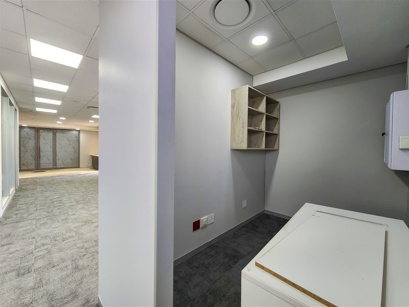 A clean, modern office space featuring neutral finishes, suspended ceiling with recessed lighting, and practical wall-mounted shelving, suitable for a professional work environment.