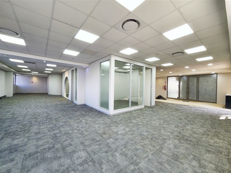 Spacious open-plan office area featuring modern glass partitions, carpeted flooring, and recessed LED lighting throughout the professional workspace.
