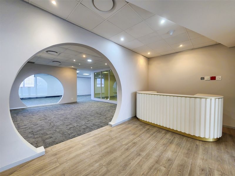 Modern office space featuring a built-in reception desk, unique architectural archway, glass partitions, and a mix of carpet and wood-look flooring.