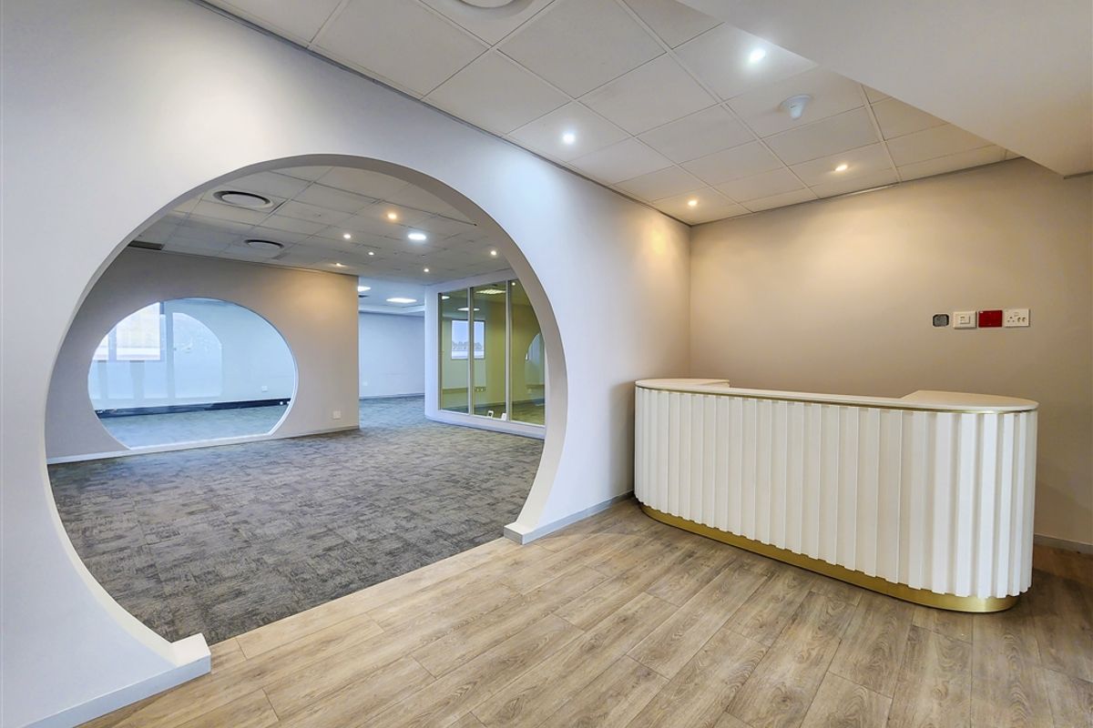 Modern office space featuring a built-in reception desk, unique architectural archway, glass partitions, and a mix of carpet and wood-look flooring.