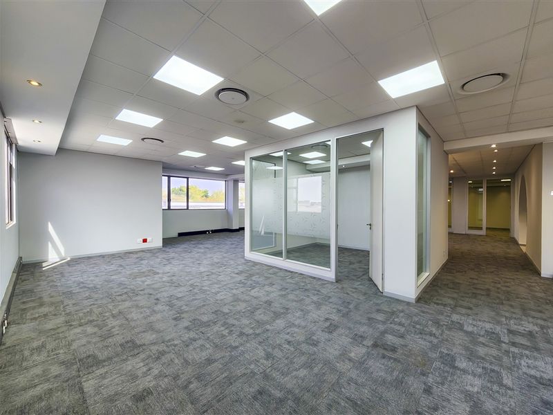 Spacious open-plan office area featuring modern glass partitioning, suspended ceilings with recessed lighting, and durable carpet tiles throughout.