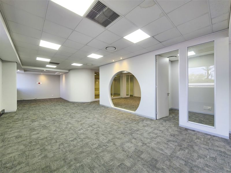 Spacious open-plan office area featuring carpet tiles, a suspended ceiling with recessed lighting, and a unique circular architectural feature with glass partitioning.