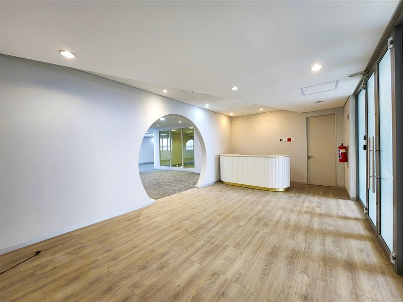Modern office entrance area featuring a built-in reception desk, wood-look laminate flooring, and a distinctive circular architectural opening leading to the main office space.