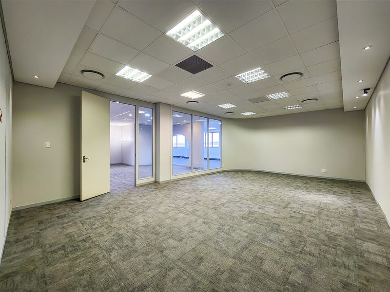 A spacious, empty office suite featuring neutral carpet tiles, a suspended ceiling with recessed lighting, and glass partition walls providing natural light.