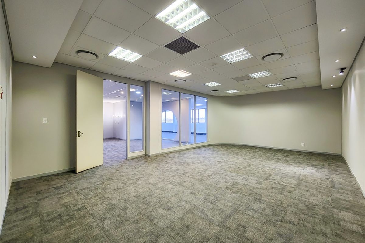 A spacious, empty office suite featuring neutral carpet tiles, a suspended ceiling with recessed lighting, and glass partition walls providing natural light.