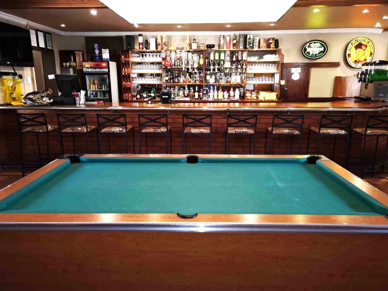 A well-equipped lodge bar area featuring a long wooden counter, extensive back bar shelving, and a central pool table.