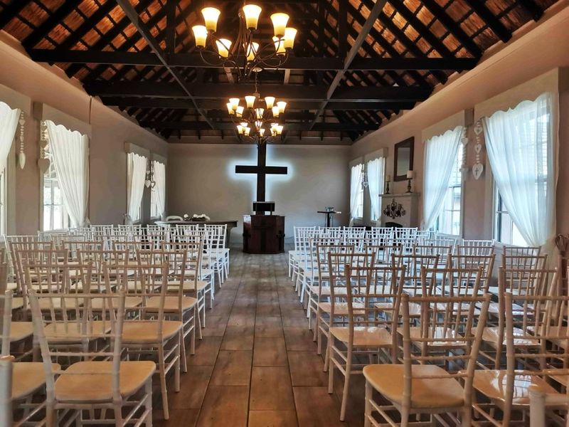 A spacious lodge chapel or event hall featuring exposed timber trusses, a thatched ceiling, tiled flooring, and a central fireplace.