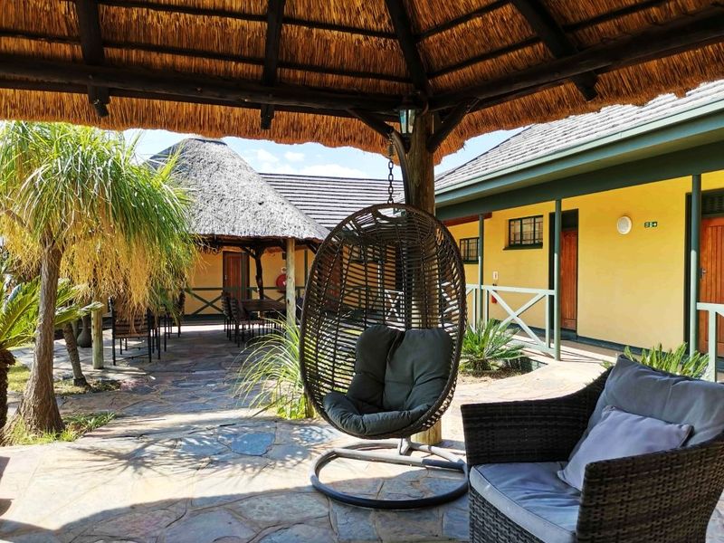 A covered outdoor patio area featuring a traditional thatch roof, stone paving, and timber structural elements, providing a shaded space for relaxation.