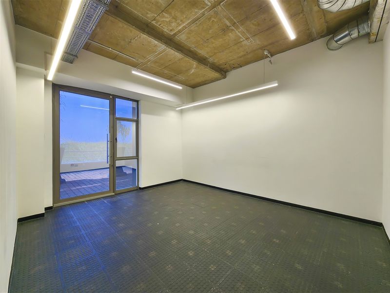 Modern empty office space featuring an exposed concrete ceiling, industrial-style linear lighting, and direct access to an outdoor balcony area.