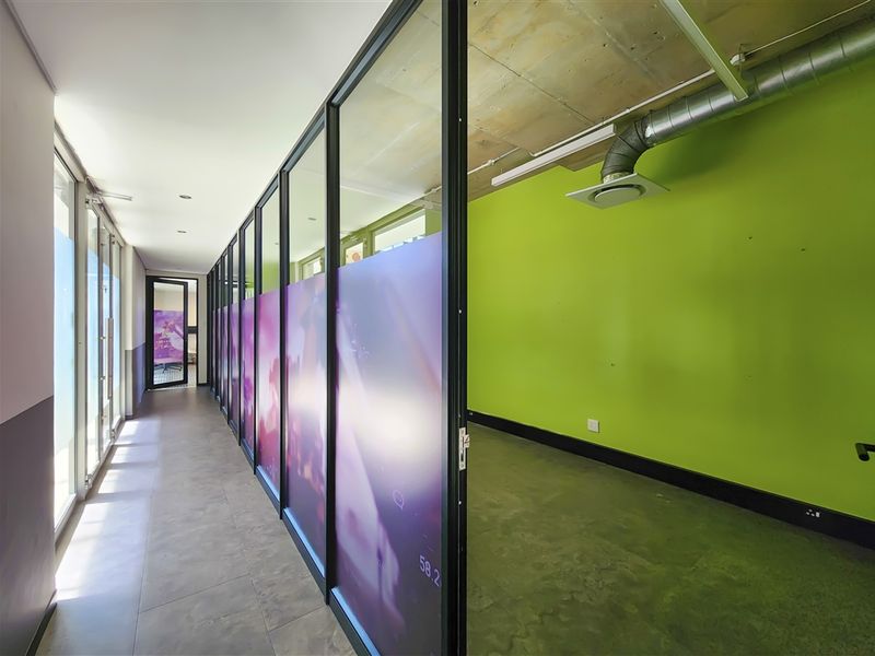 Modern office space featuring glass partitions, exposed industrial-style ceiling with ducting, and tiled flooring, offering a bright and contemporary work environment.