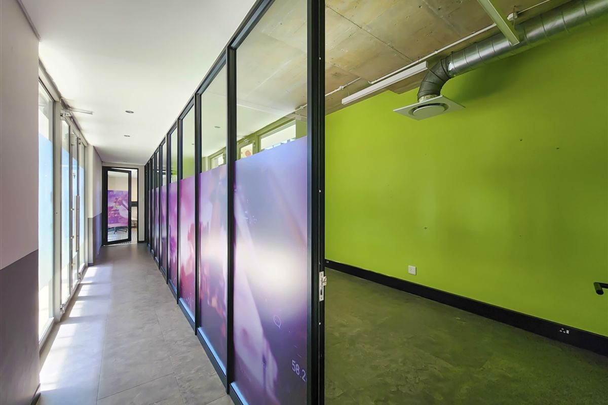 Modern office space featuring glass partitions, exposed industrial-style ceiling with ducting, and tiled flooring, offering a bright and contemporary work environment.