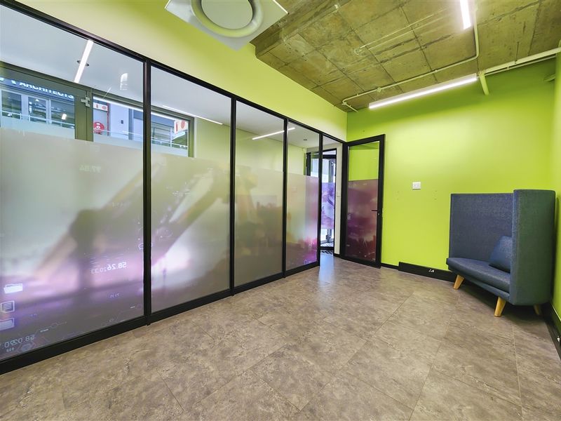 Modern office space featuring an exposed concrete ceiling, tiled flooring, and a glass partition wall with frosted privacy film.