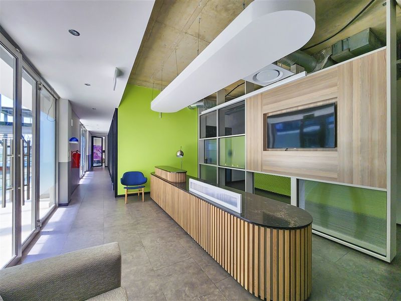 Modern office reception area featuring a custom wood-slat desk, exposed concrete ceiling, and floor-to-ceiling glass partitions providing natural light.