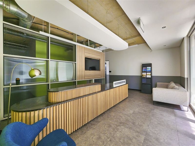 Modern office reception area featuring a custom slatted timber desk, exposed concrete ceiling, and contemporary glass partitioning with integrated display shelving.