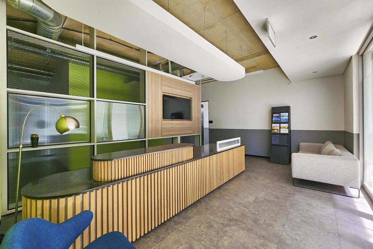 Modern office reception area featuring a custom slatted timber desk, exposed concrete ceiling, and contemporary glass partitioning with integrated display shelving.