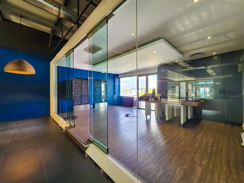 Modern office space featuring glass partitions, exposed industrial ceilings, and high-quality laminate flooring, offering a bright and professional work environment.