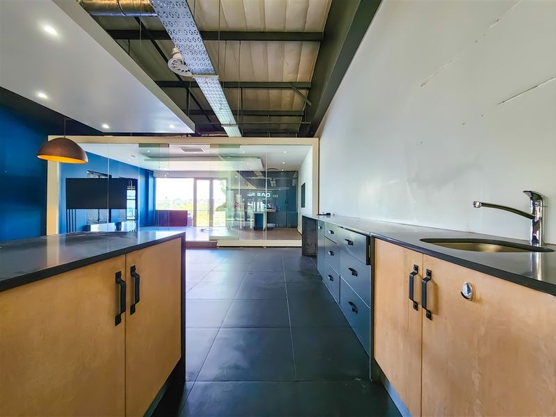 Modern office space featuring a kitchenette area with built-in cabinetry, stainless steel sink, exposed industrial ceiling, and glass partitions for an open-plan feel.