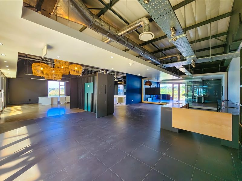 Spacious open-plan office area featuring industrial-style exposed ceilings, modern glass partitions, tiled flooring, and a built-in reception desk.