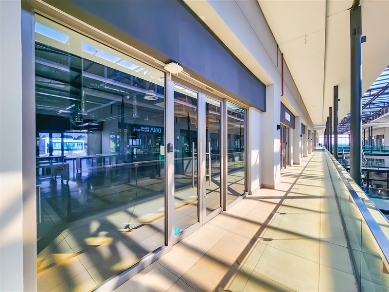 Modern office entrance with a glass facade and a spacious tiled walkway, featuring clean lines and contemporary architectural finishes.