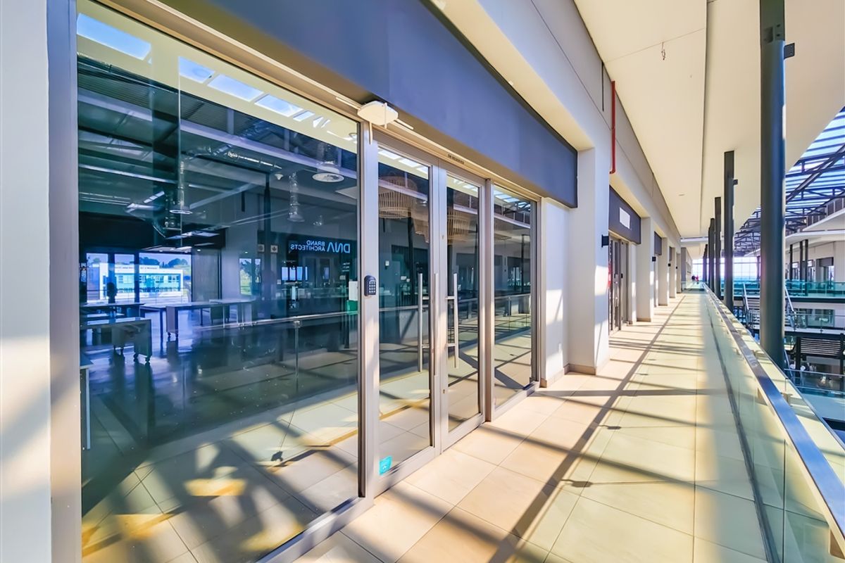 Modern office entrance with a glass facade and a spacious tiled walkway, featuring clean lines and contemporary architectural finishes.