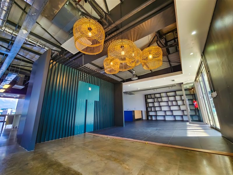Modern open-plan office space featuring exposed industrial ceilings, contemporary pendant lighting, built-in shelving, and a mix of polished concrete and tiled flooring.