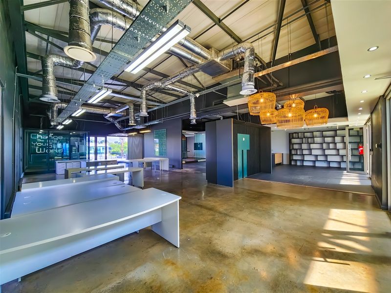 Spacious open-plan office featuring industrial-style exposed ductwork, polished concrete floors, and modern glass partitioning with integrated shelving units.