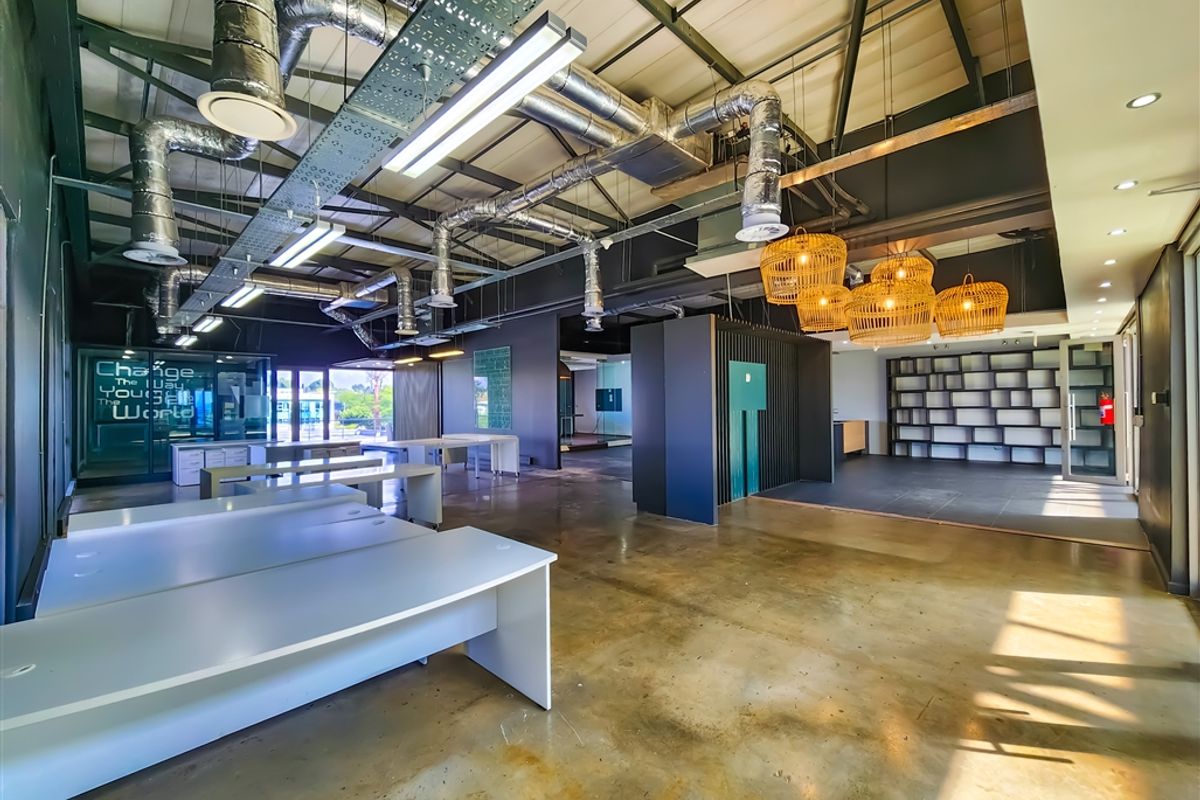 Spacious open-plan office featuring industrial-style exposed ductwork, polished concrete floors, and modern glass partitioning with integrated shelving units.