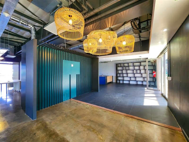 Modern open-plan office space featuring exposed industrial ceiling, decorative pendant lighting, built-in shelving, and a striking corrugated metal feature wall.