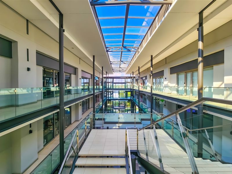 Modern multi-level office atrium featuring a large glass skylight, contemporary glass balustrades, and a central tiled staircase connecting the office suites.