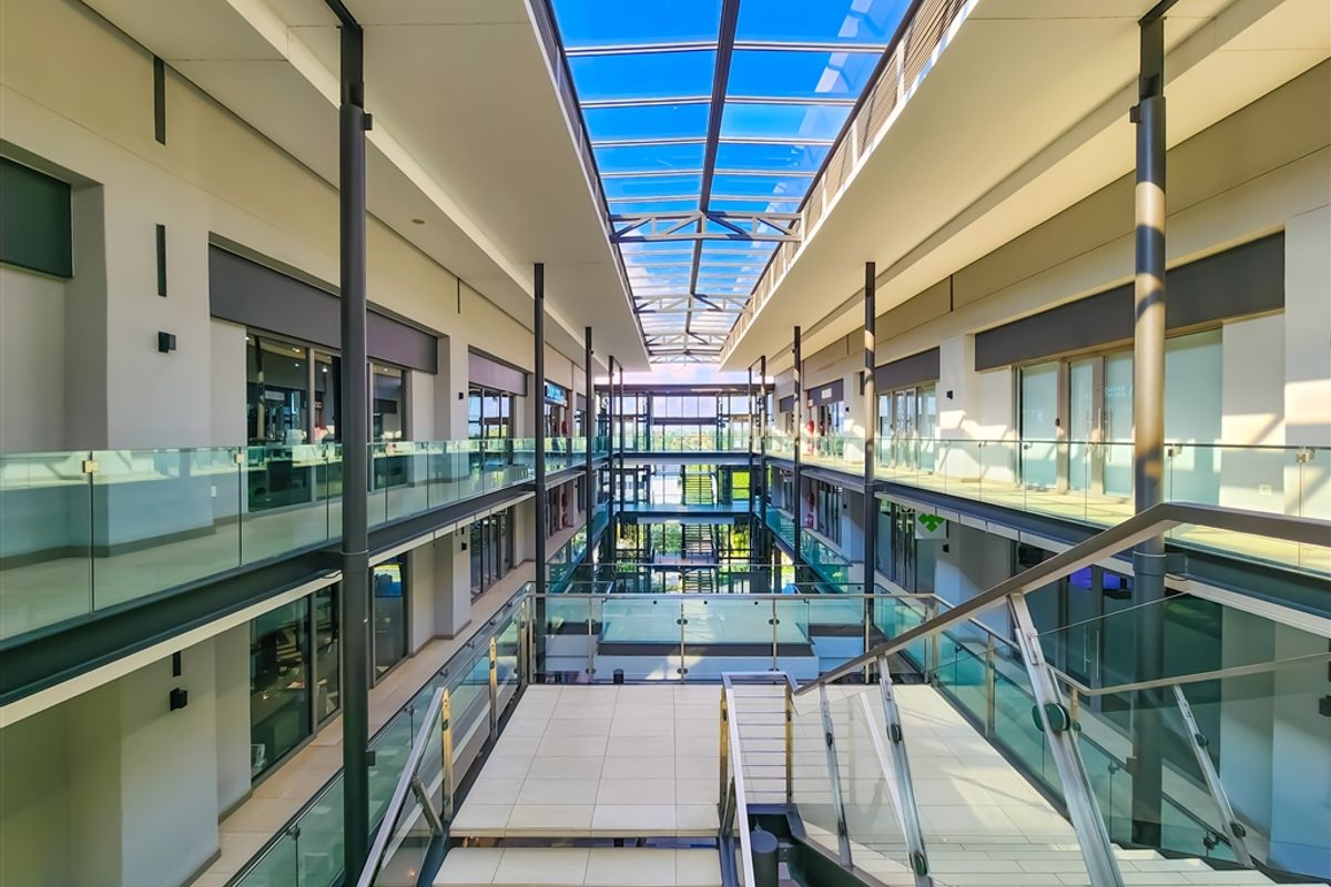 Modern multi-level office atrium featuring a large glass skylight, contemporary glass balustrades, and a central tiled staircase connecting the office suites.