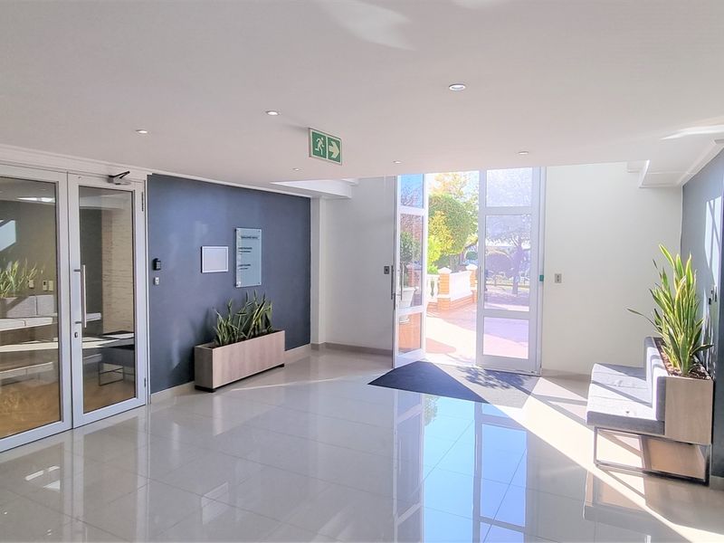Modern office building entrance lobby featuring polished tile flooring, glass partition walls, and bright natural light from the double glass entrance doors.
