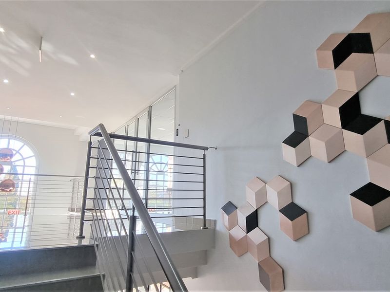 Modern office hallway featuring a stainless steel balustrade, tiled flooring, recessed lighting, and a large arched window providing natural light.