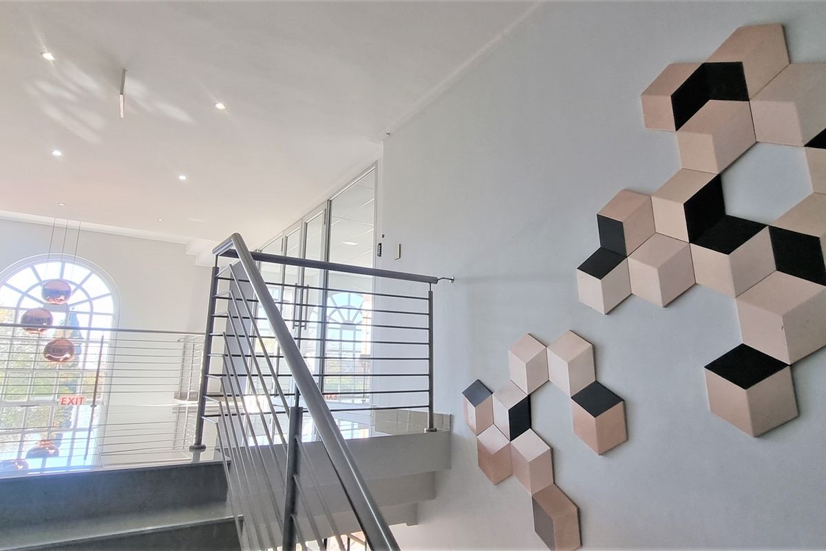 Modern office hallway featuring a stainless steel balustrade, tiled flooring, recessed lighting, and a large arched window providing natural light.