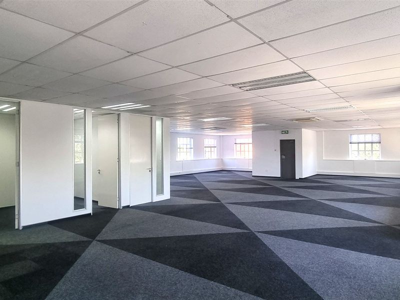 A spacious, open-plan office area featuring a suspended ceiling, recessed lighting, and patterned carpet tiles, with several partitioned internal office rooms.