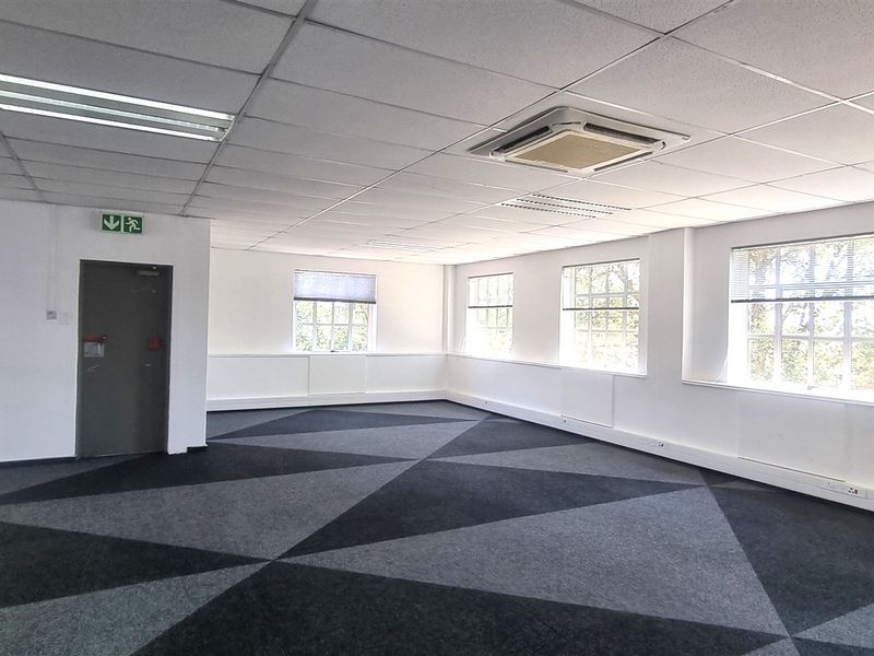 A spacious, open-plan office area featuring a suspended ceiling, recessed lighting, integrated cassette air conditioning, and modern patterned carpet tiles.