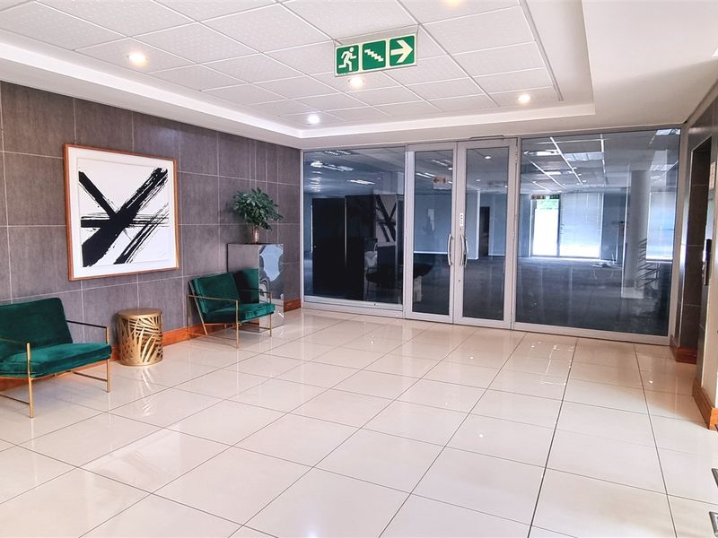 Modern office building entrance lobby featuring polished tiled flooring, a contemporary feature wall, and glass doors leading to the main office area.