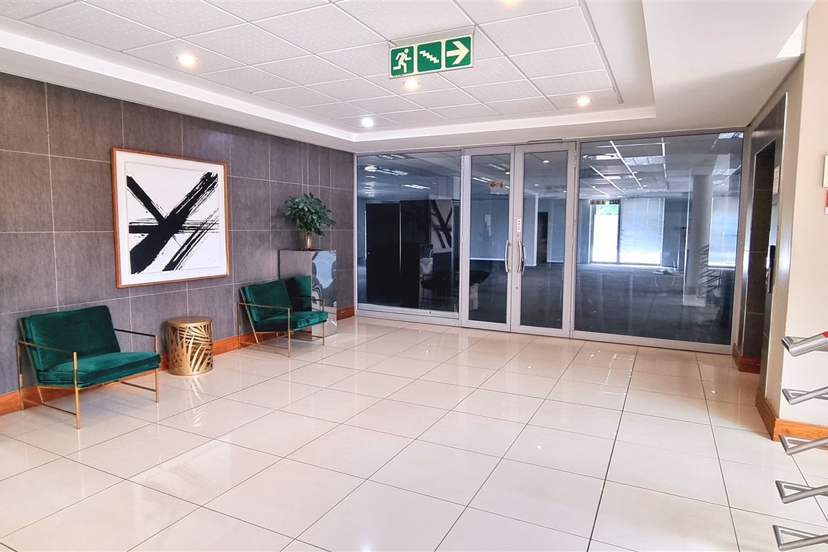 Modern office building entrance lobby featuring polished tiled flooring, a contemporary feature wall, and glass doors leading to the main office area.