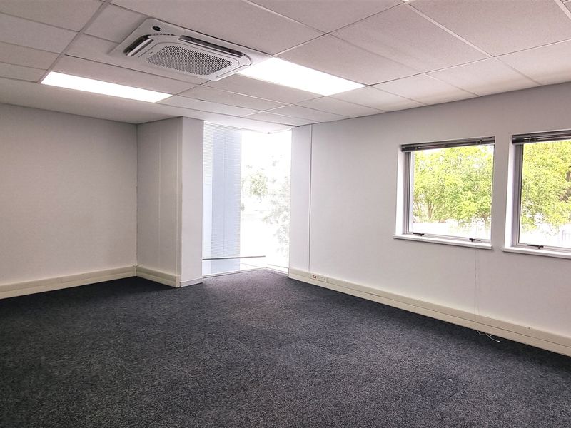 A vacant, well-lit office space featuring a suspended ceiling, integrated air conditioning, and large windows providing natural light and exterior views.