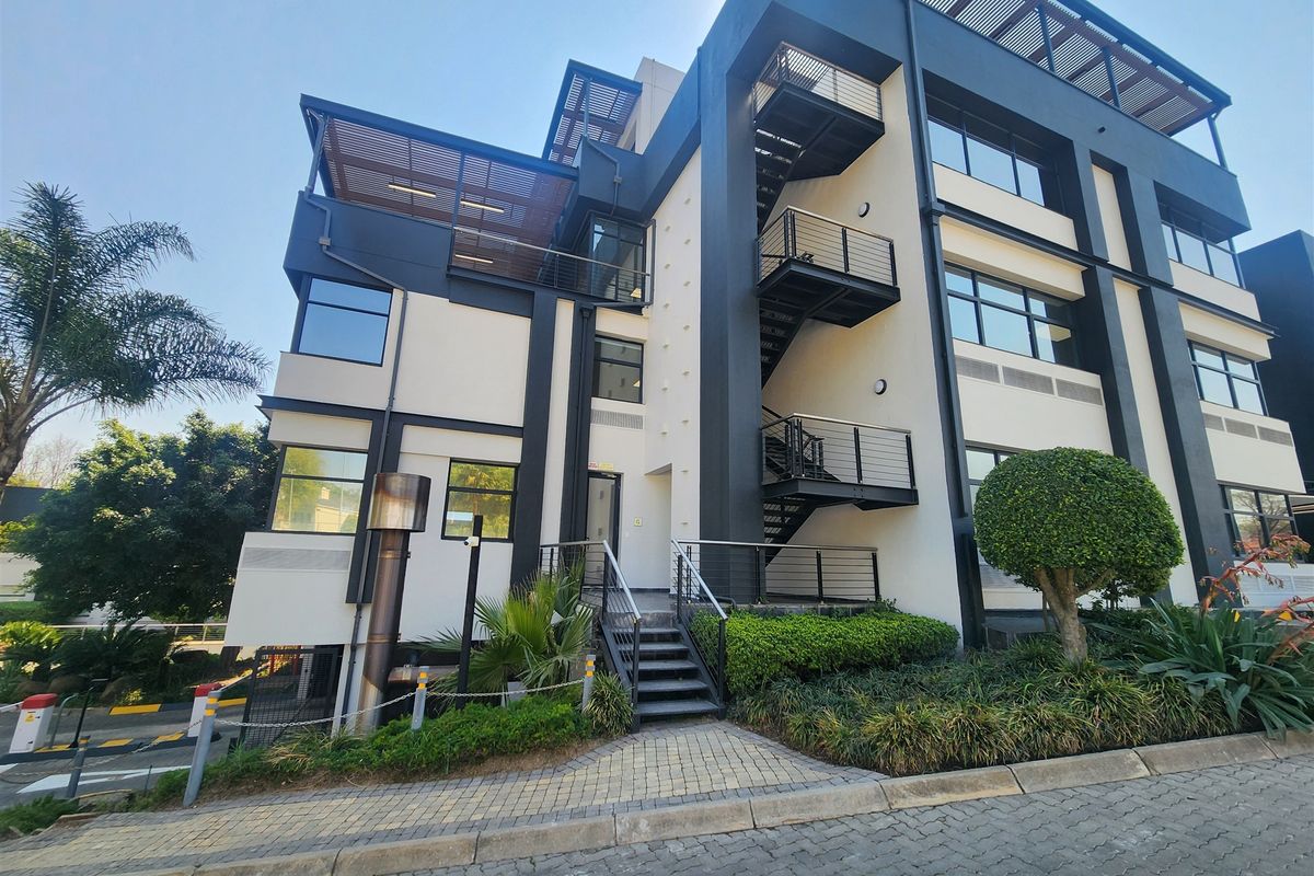 Modern multi-story office building featuring a contemporary facade, external steel staircase, balconies with pergolas, and well-maintained landscaped surroundings.