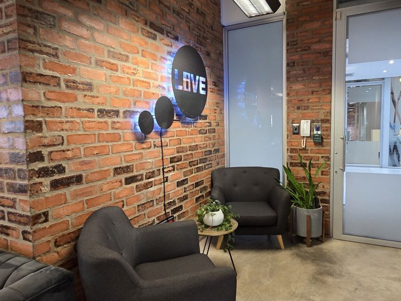 A modern office reception area featuring an exposed brick wall, concrete flooring, and a glass partition door.