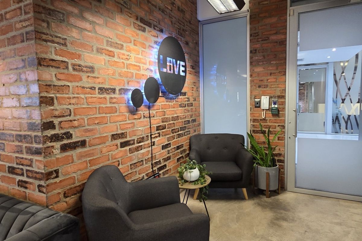 A modern office reception area featuring an exposed brick wall, concrete flooring, and a glass partition door.