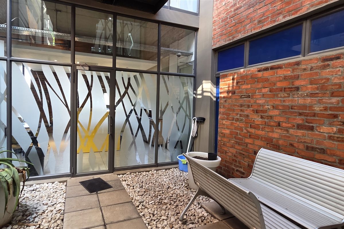 A private courtyard area featuring an exposed brick wall, paved walkway, pebble landscaping, and a modern glass facade with decorative frosted film.