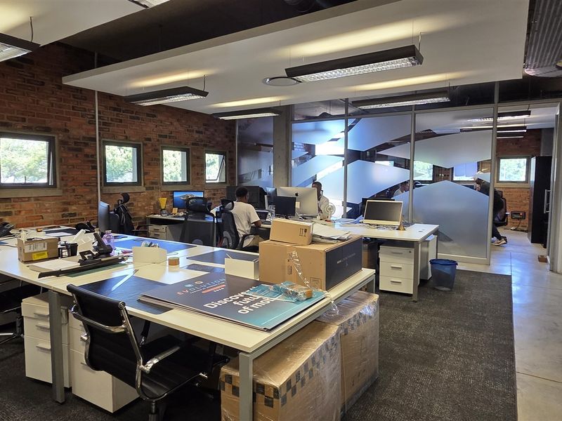 Modern open-plan office space featuring exposed brick walls, polished concrete floors, and glass partitions with frosted privacy detailing.