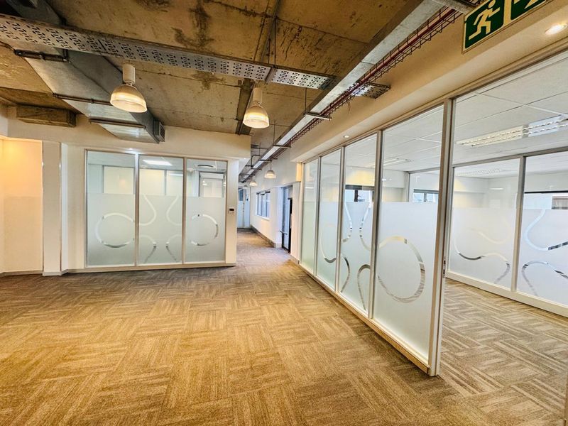Modern open-plan office space featuring exposed concrete ceilings, glass partitioned offices with privacy film, and durable carpet tile flooring.