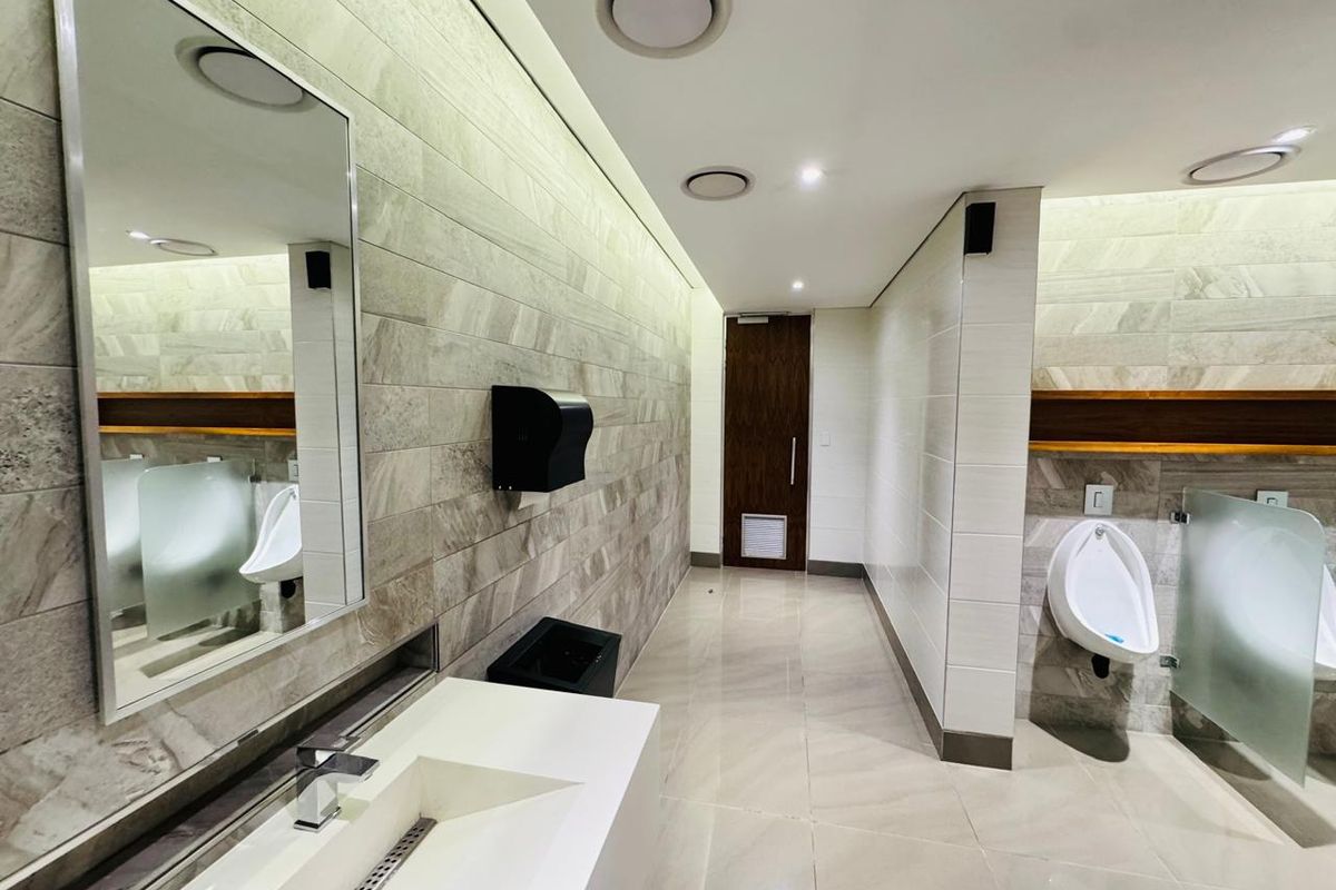 Modern, well-maintained office restroom featuring high-quality tiled finishes, integrated vanity sink, and wall-mounted urinals with privacy partitions.