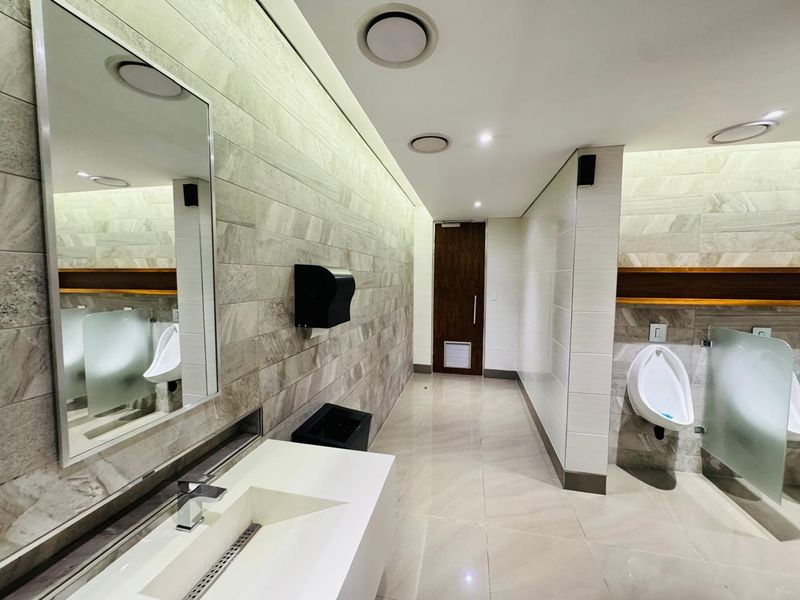 Modern, well-maintained office restroom featuring high-quality tiled finishes, integrated vanity sink, and wall-mounted urinals with privacy partitions.
