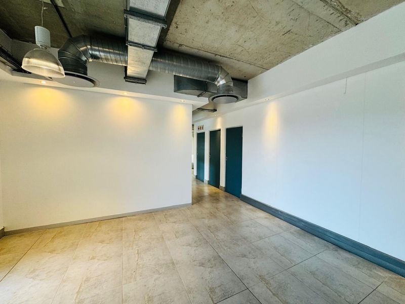 Modern open-plan office space featuring an industrial aesthetic with exposed concrete ceilings, exposed HVAC ducting, tiled floors, and recessed lighting.