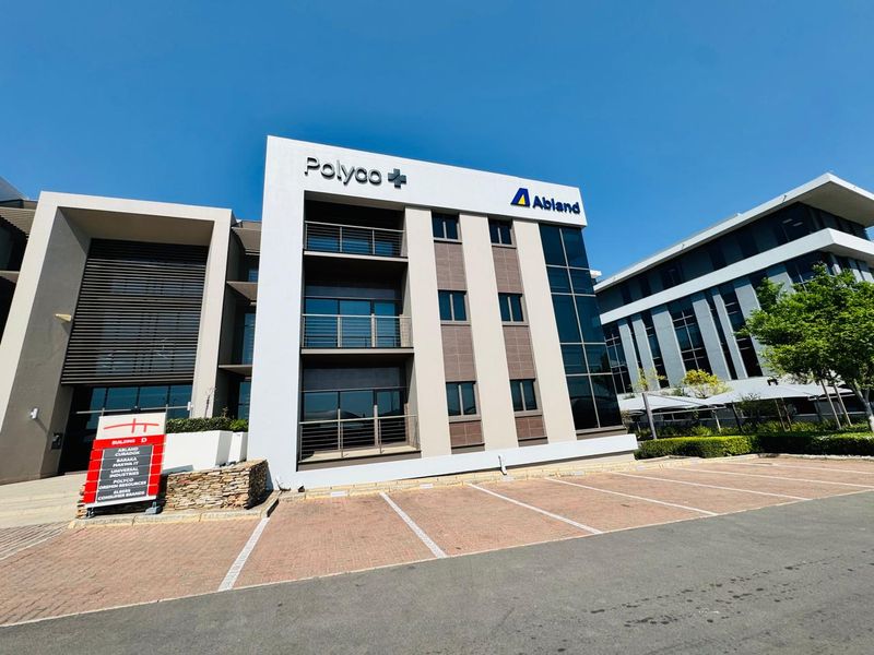 Modern multi-story office building exterior featuring a paved parking area, glass facade, and prominent corporate signage.