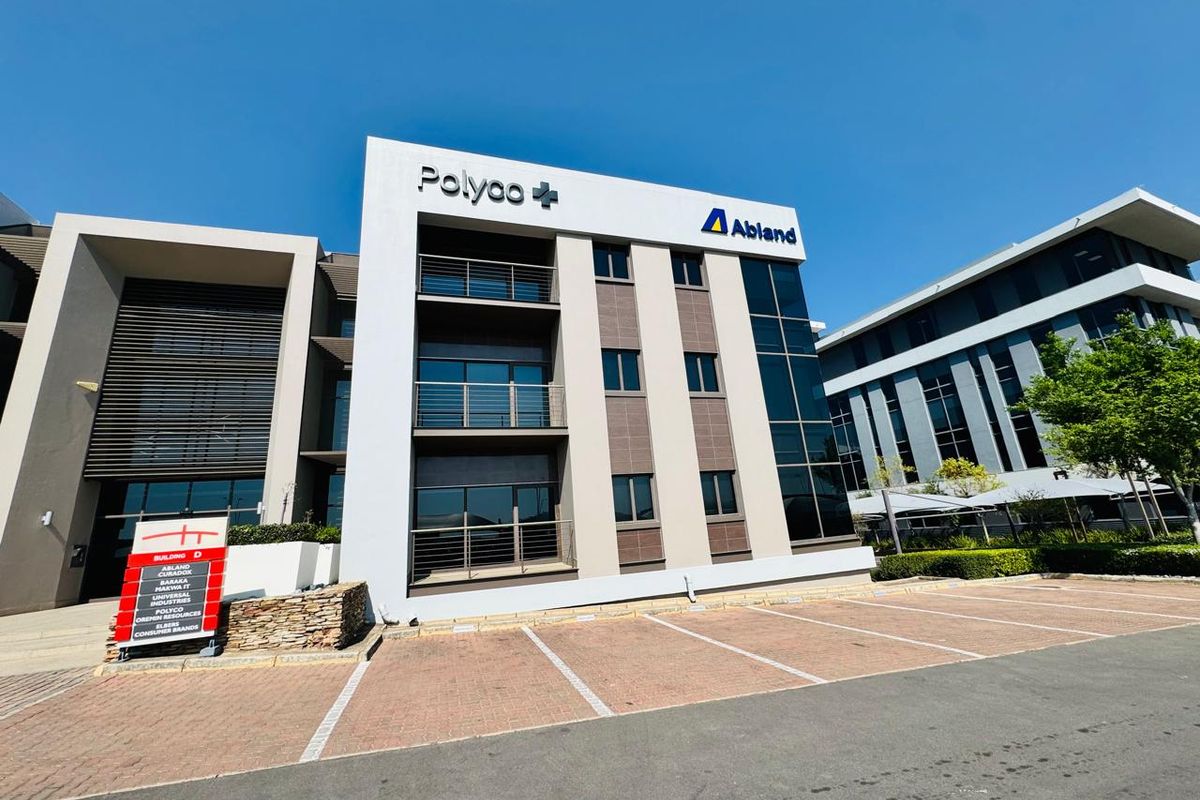 Modern multi-story office building exterior featuring a paved parking area, glass facade, and prominent corporate signage.