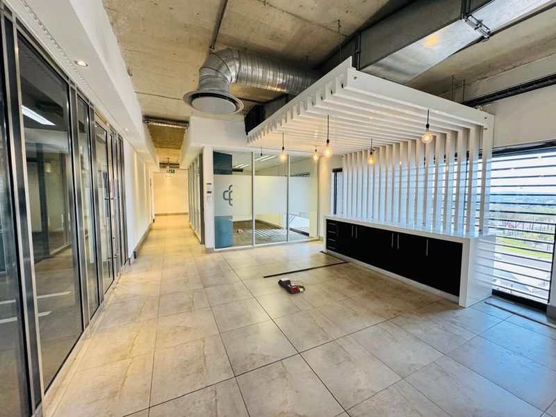 Modern open-plan office space featuring exposed industrial ceilings, glass partitions, tiled flooring, and a custom built-in reception or kitchenette area with slatted timber detailing.